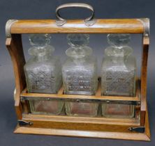 An Edwardian oak and silver plated tantalus, with four cut glass square section decanters and facete