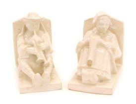 A pair of 1920s Henry Delcourt Faience bookends, decorated with a gentleman, piper, and a lady, 11cm