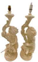 A pair of cream painted composition table lamps, each modelled in the form of a putto holding a corn