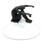 A bronzed resin coffee table, modelled in the form of a nude seated on a cushion holding the oval gl