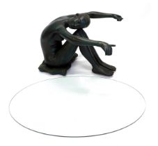 A bronzed resin coffee table, modelled in the form of a nude seated on a cushion holding the oval gl
