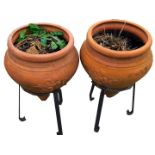 A pair of terracotta urn planters, each on metal stand, with rose detail, 66cm high, 35cm diameter.