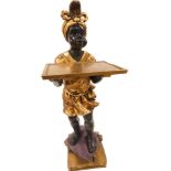 A cold painted resin Blackamore figure, picked out in gilt, standing on a purple cushion holding a t