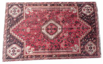 A Shiraz rug, decorated with a medallion surrounded by geometric devices, birds, etc., on a red grou