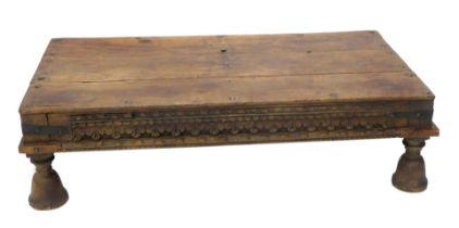 An Eastern hardwood table, the rectangular planked top with iron bolts or nails, above a carved frie