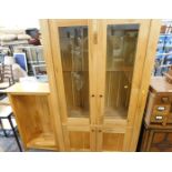 A beech effect display cabinet, with glazed doors and two cupboard base, and a matching bookcase. (2