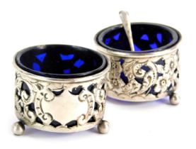 A pair of George V silver salts, each with blue glass liners, vacant shield with pierced floral deco