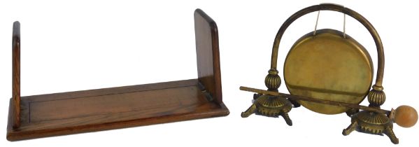 An early 20thC oak sliding book rack, 34cm wide, together with a brass dinner gong, 20cm high. (2)