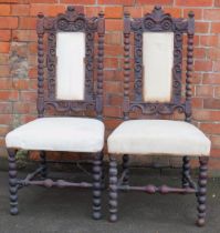Two 19thC oak hall chairs, each with a carved floral scroll back, with cream cushioned seats.