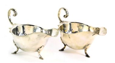 A pair of silver plated sauce boats, with fluted border and scroll capped handle, on tripod feet, be
