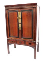 A Chinese two door cabinet, enclosed by fielded panelled doors, with ebonised outline, above three d