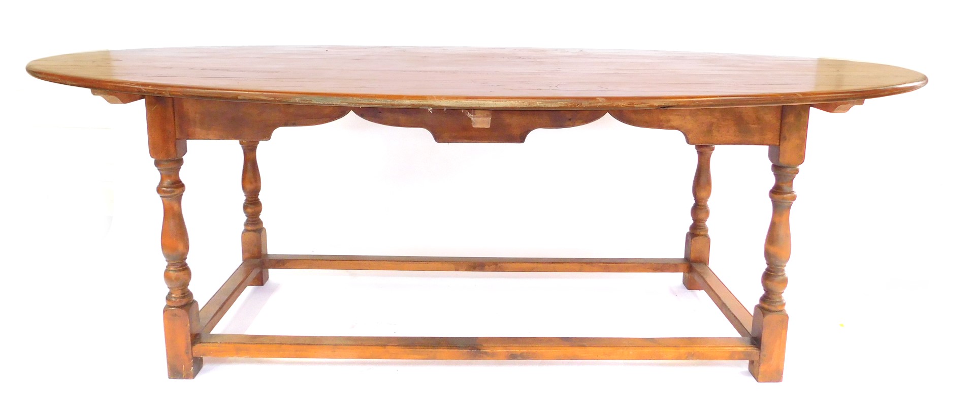 A large fruit wood oval kitchen table, the plank top, shaped apron on turned supports with stretcher