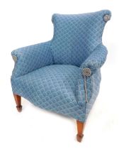 An early 20thC low seated upholstered armchair, with blue scale pattern upholstery, on square tapere