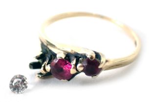 A three stone dress ring, set with two rubies and one loose white stone, on a yellow metal band stam