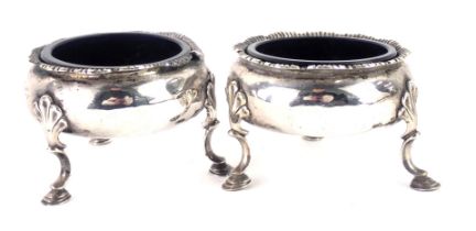 A pair of 18thC silver salts, with petalated border and shell tripod feet, with blue glass liners, f