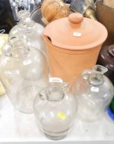 Four glass Demijohns and a terracotta jar and cover.