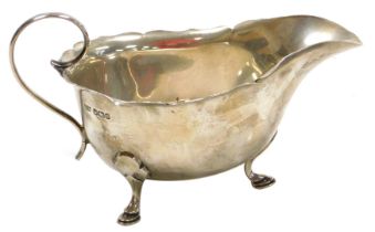 A George V silver sauce boat, with a scroll handle, raised on three hoof feet, Mappin and Webb, Shef