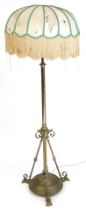 An early 20thC brass standard lamp, with a tasselled silk shade, 145cm high. (AF) Buyer Note: WARNIN