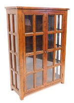 A 20thC mango wood bookcase, with two glazed doors, enclosing three shelves, raised on stiles, 145cm