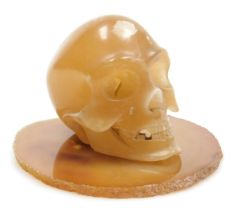 A yellow quartz carving of a skull, 10cm deep, on an agate base. (2)