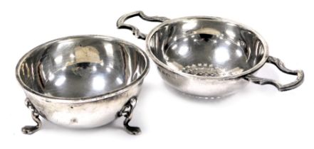 A George VI silver twin handled tea strainer and bowl, raised on three shell capped paw feet, Birmin