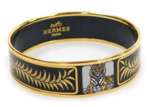 An Hermes gold plated and enamel bangle, decorated with tigers, crowns and wreaths, on a black groun