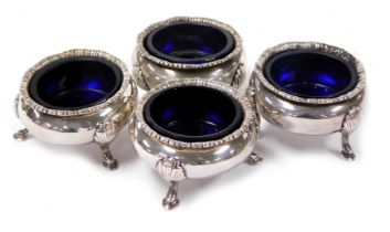 A set of four Edwardian silver circular salts, raised on three leaf capped paw feet, with blue glass
