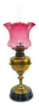 A 19thC brass oil lamp, with floral etched cranberry shade, brass reservoir, on turned column, on bl