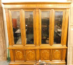 A 20thC hardwood display cabinet, the top with a moulded edge above four glazed cupboard doors enclo