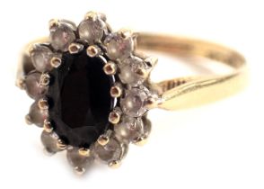 A 9ct gold cluster ring, the oval cluster centred by a dark blue stone surrounded by CZ's, in a rais