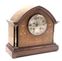 An Edwardian oak mantel clock, with arched top and boxwood tulip inlay and silvered dial, on columne