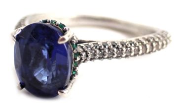 A dress ring, set with oval cut sapphire, surrounded by tiny emeralds to a raised shank setting with