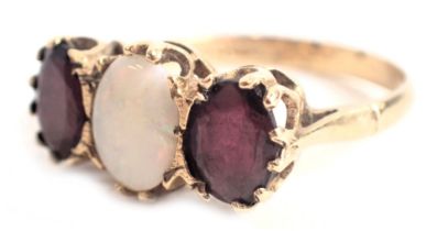 A 9ct gold dress ring, set with two garnets and an opal, each oval cut, in raised claw basket settin