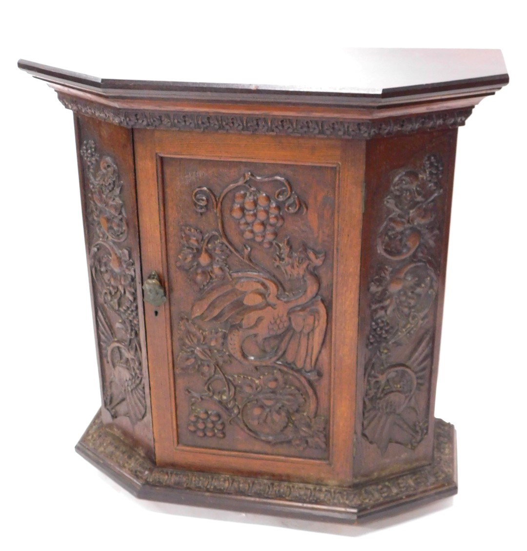 A carved oak side cabinet, with canted corners, the door decorated with grapes, leaves, etc., 89cm h