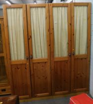 Two pine double wardrobes, each with a glazed top door and internal curtain on block base.