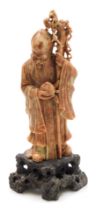 A Chinese soapstone figure of Shou Lao, God of Longevity, modelled standing holding a staff and a pe
