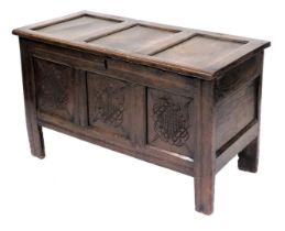 An 18thC oak coffer, with a triple panelled lid, over a front with carved decoration, raised on stil