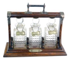 A late 19thC oak and plate mounted Tantalus, with three cut glass decanters and stoppers, each with