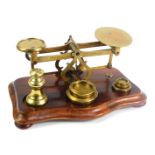 A set of vintage brass postal scales, with weights, raised on a serpentine base, 19cm wide.