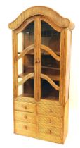 A cane reeded display cabinet, with an arched top above two panelled doors and six short drawers, 20