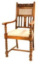 An early 20thC oak open armchair, with a part woven cane panelled back and carved floral top rail, w