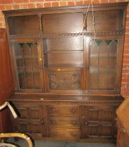 An oak cabinet, the top with a recess above two glazed doors, with further recesses and a carved fal