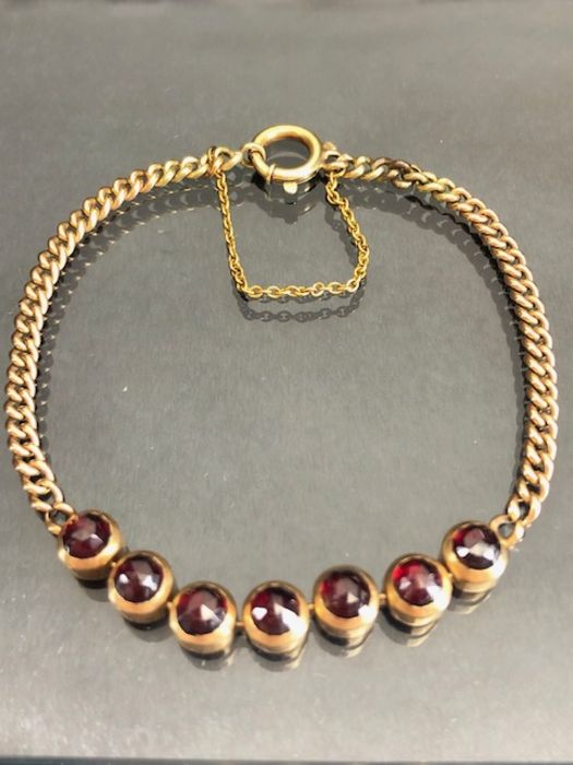 9ct Gold Bracelet of link design and set with seven faceted garnets and with safety chain (total