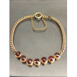 9ct Gold Bracelet of link design and set with seven faceted garnets and with safety chain (total