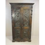 Heavily carved two door wardrobe with carved panels and shelf and hook to interior, arts ands crafts