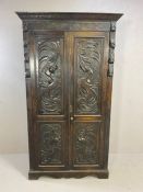 Heavily carved two door wardrobe with carved panels and shelf and hook to interior, arts ands crafts