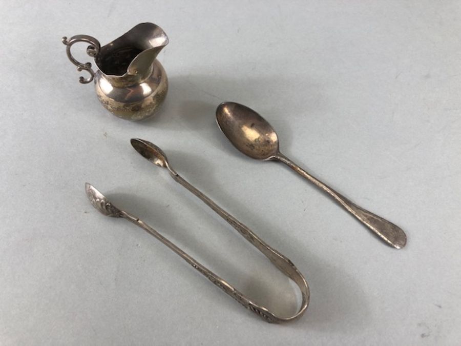 Three silver hallamrked items to include sugar nips a miniature cream jug and a spoon