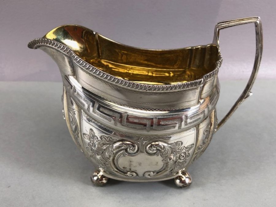 Silver hallmarked jug on four bun feet with gold gilt interior and repoussé floral decoration