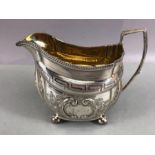 Silver hallmarked jug on four bun feet with gold gilt interior and repoussé floral decoration