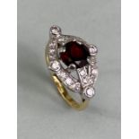 Unmarked yellow and white gold ring set with a central red faceted Gemstone in four claws and framed